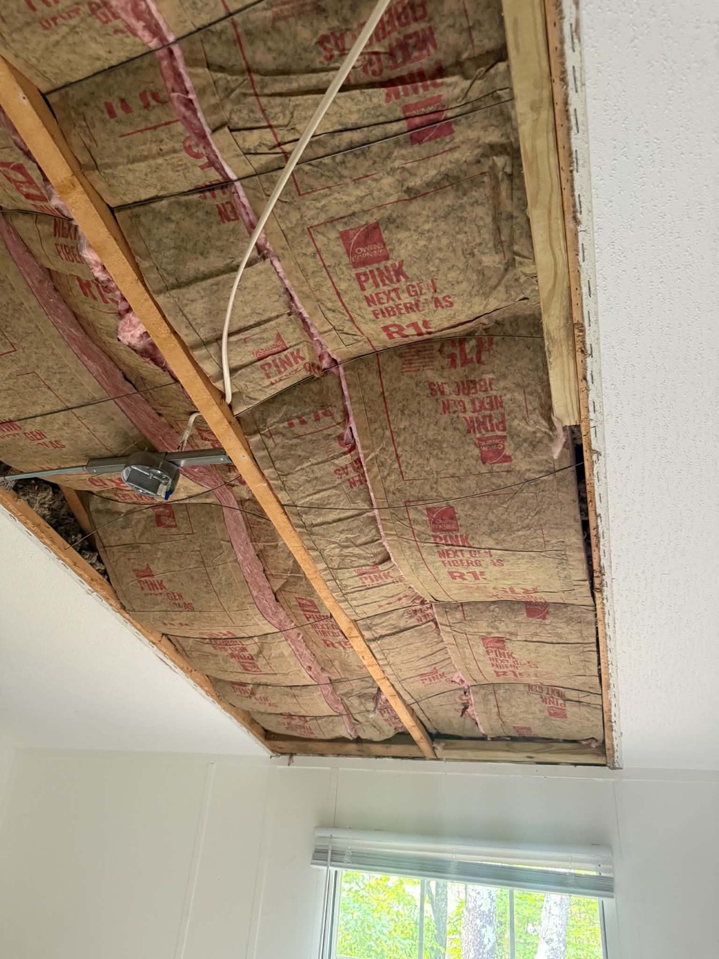 Close view of kraft-faced insulation batts and wiring between ceiling joists in an opened ceiling