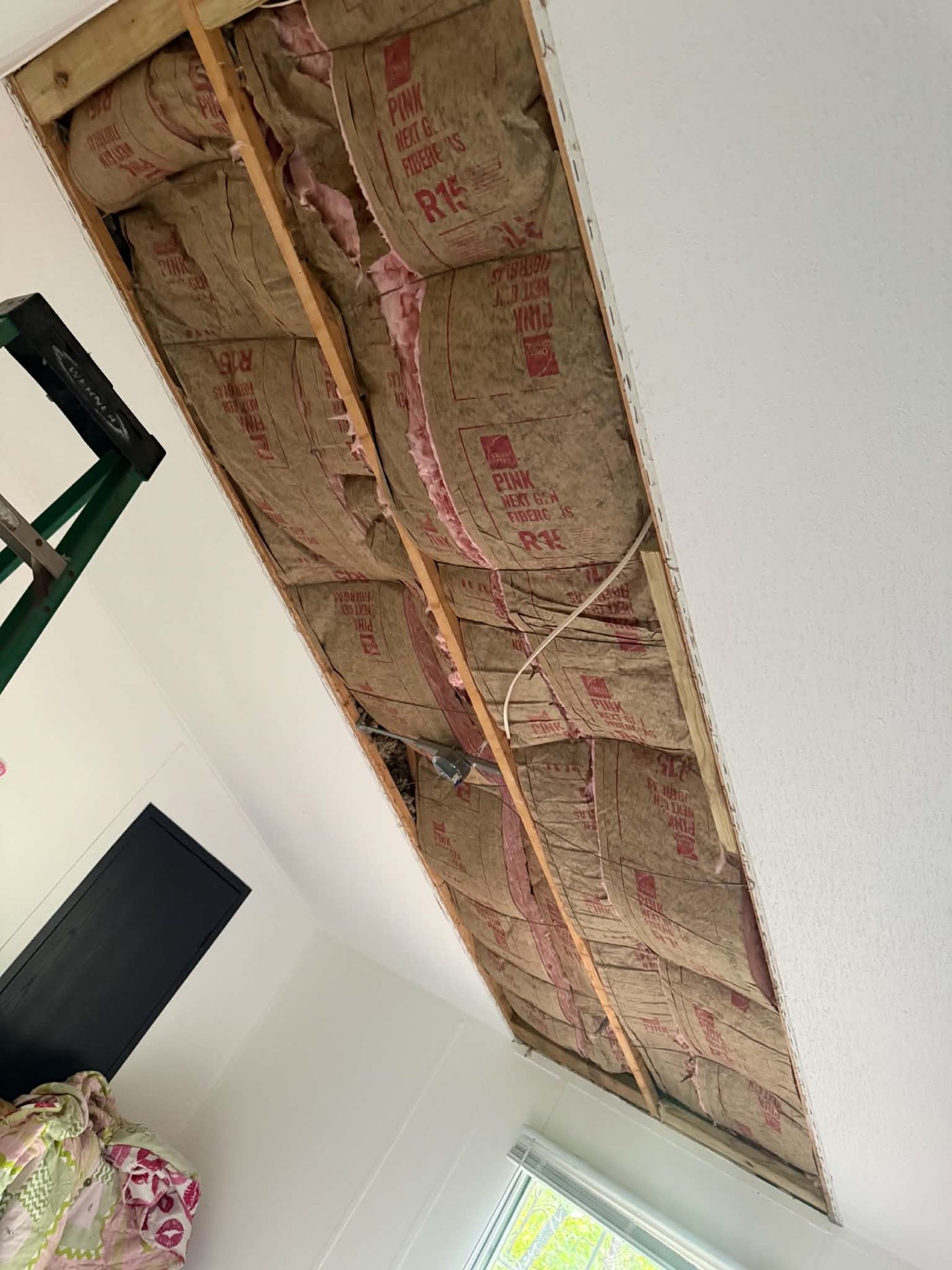 Wide view of an opened ceiling section showing parallel joists and batt insulation between them