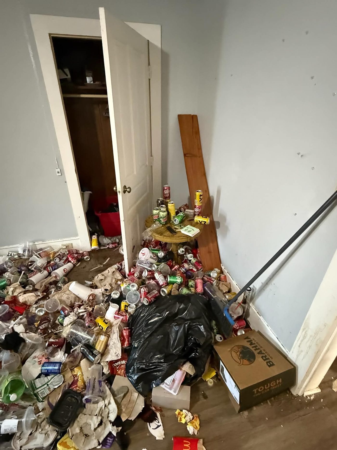 Corner of a room with drink cans and food waste piled against a closet door, blocking it from opening