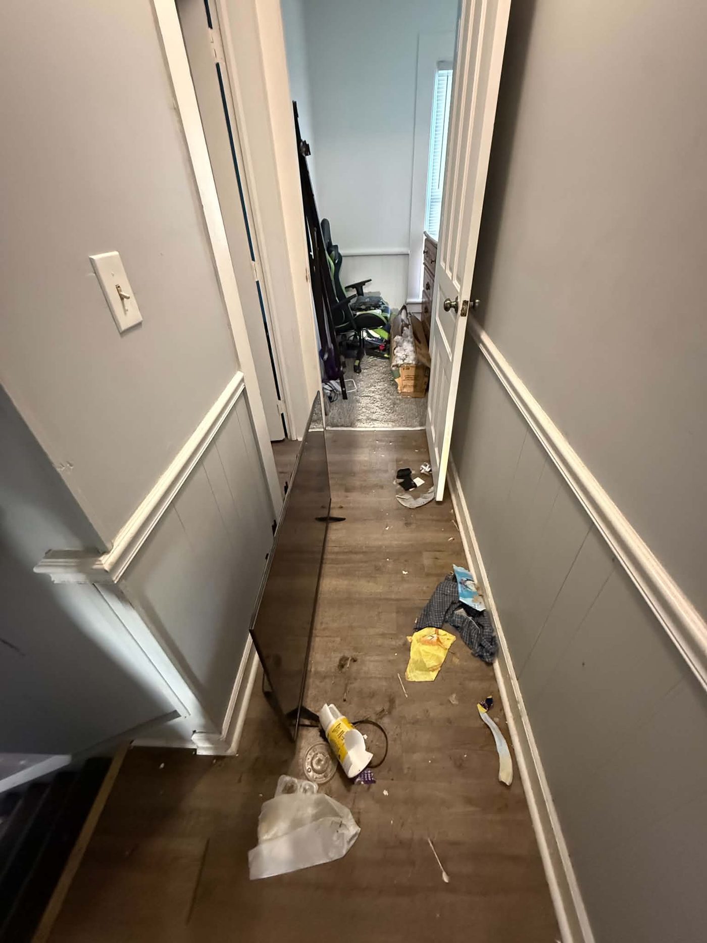 Narrow hallway with a television leaning against the wall and scattered debris on the floor