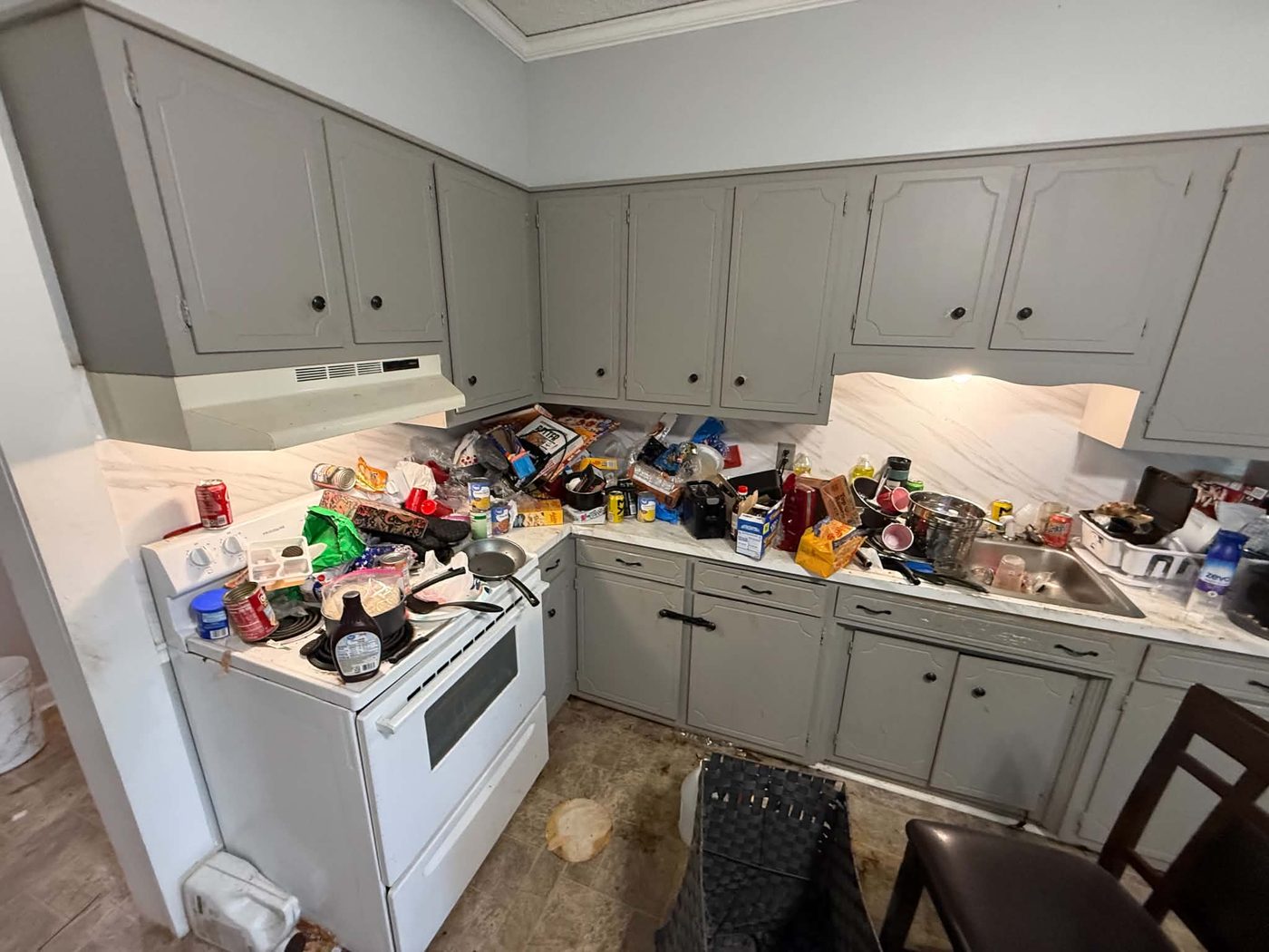 Kitchen with counters, stove and sink covered in packaging, cans, cookware and food waste